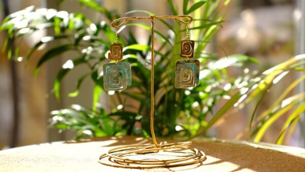 Pendientes/Aretes inspirados en la simbología Wayuu del pueblo aborigen Colombiano. Aretes elaborados de manera artesanal patinados bajo la reacción natural del metal y el ambiente, complementados con sutiles trazos de pintura manual. Material Latón con pasantes chapados en oro de 18 Kt de 1,2 mm. Medidas aproximadas: 7,05 cm altura total. Ancho de figura pequeña 2 cm y de figura grande 3 cm. El color de los pendientes en la parte de patinada es azul turquesa. Dependiendo el ángulo y la luz de donde los estes viendo, puede verse con un tono un poco más azul celeste. La simbología de estos pendientes representan purificación, protección de la verdad y eternidad.