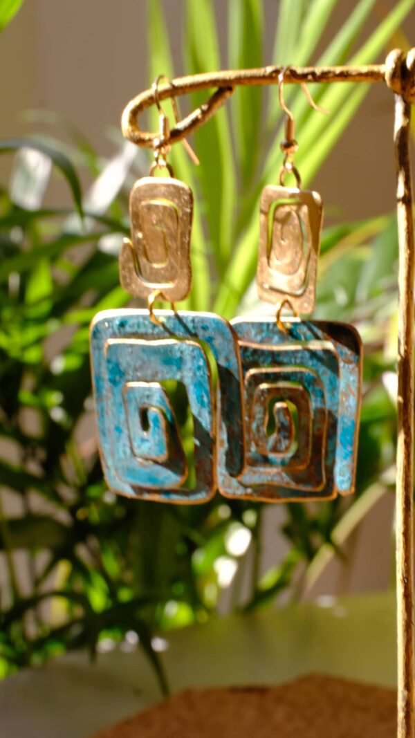 Pendientes/Aretes inspirados en la simbología Wayuu del pueblo aborigen Colombiano. Aretes elaborados de manera artesanal patinados bajo la reacción natural del metal y el ambiente, complementados con sutiles trazos de pintura manual. Material Latón con pasantes chapados en oro de 18 Kt de 1,2 mm. Medidas aproximadas: 7,05 cm altura total. Ancho de figura pequeña 2 cm y de figura grande 3 cm. El color de los pendientes en la parte de patinada es azul turquesa. Dependiendo el ángulo y la luz de donde los estes viendo, puede verse con un tono un poco más azul celeste. La simbología de estos pendientes representan purificación, protección de la verdad y eternidad.