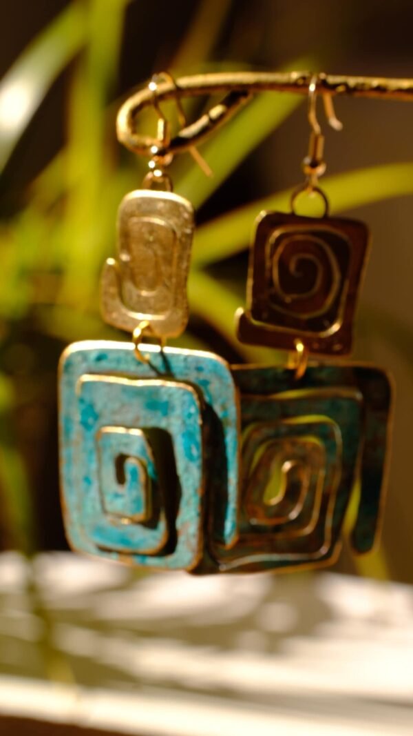 Pendientes/Aretes inspirados en la simbología Wayuu del pueblo aborigen Colombiano. Aretes elaborados de manera artesanal patinados bajo la reacción natural del metal y el ambiente, complementados con sutiles trazos de pintura manual. Material Latón con pasantes chapados en oro de 18 Kt de 1,2 mm. Medidas aproximadas: 7,05 cm altura total. Ancho de figura pequeña 2 cm y de figura grande 3 cm. El color de los pendientes en la parte de patinada es azul turquesa. Dependiendo el ángulo y la luz de donde los estes viendo, puede verse con un tono un poco más azul celeste. La simbología de estos pendientes representan purificación, protección de la verdad y eternidad.