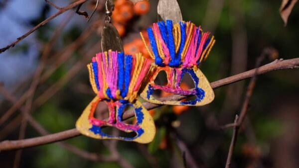 Pendientes artesanales pintados a mano con rostro de figura aborigen con hilos de colores.